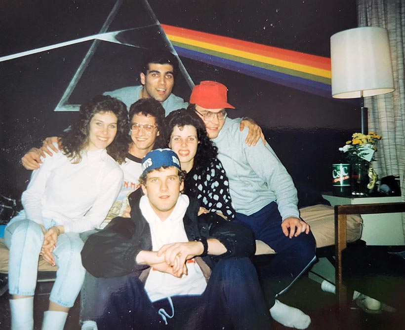 Six students posing in front of a wall painted with the Dark Side of the Moon album cover.