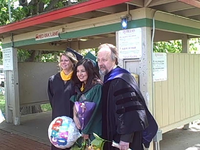 A graduate flanked by two professors, all in graduation regalia.