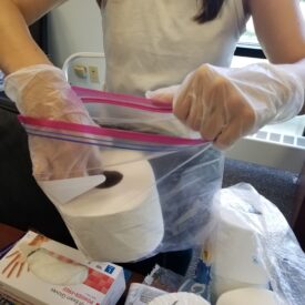Staff person putting roll of toilet paper in ziplock bag for care package.